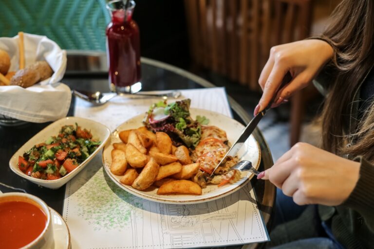 A person cutting into a delicious meal of chicken and potatoes with a salad.